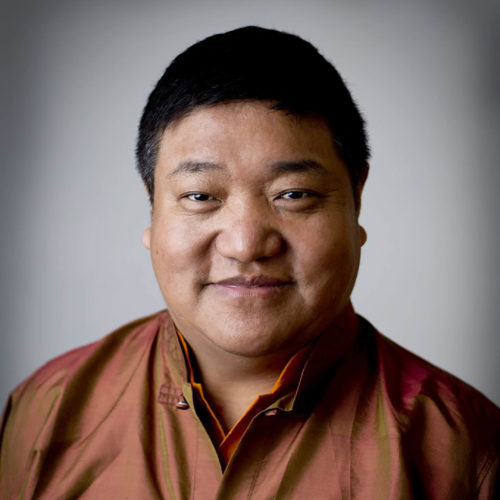 Portrait of a man wearing a burnt orange shirt, slightly smiling.